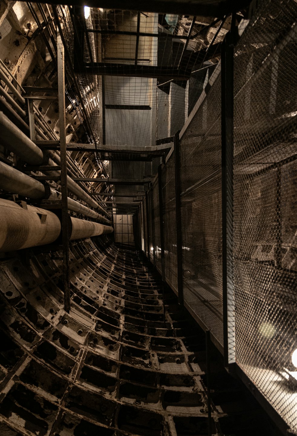 Tunnel industriale con tubi metallici e recinzione in rete metallica.