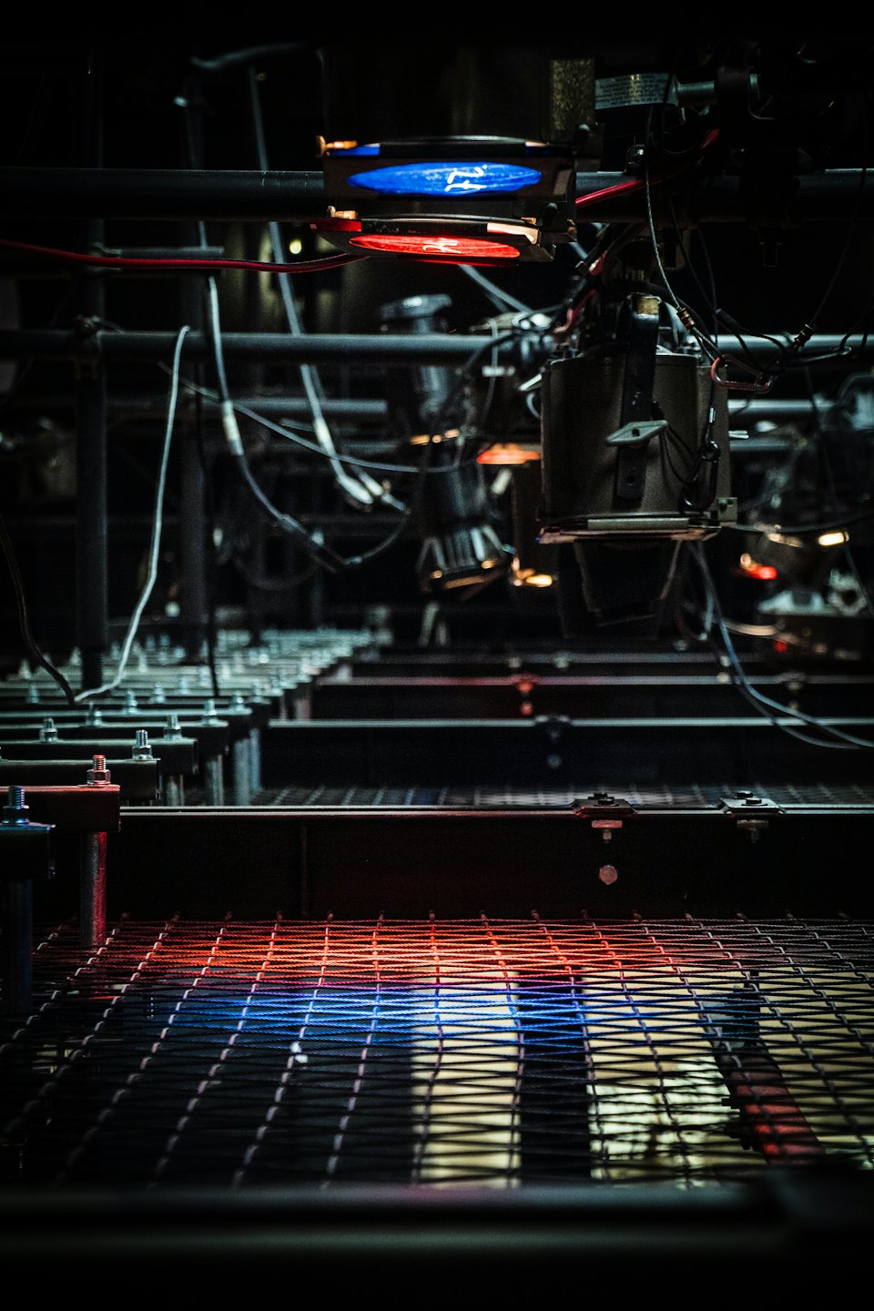 Macchinario industriale intricato con luci rosse e blu su un pavimento di grata metallica.