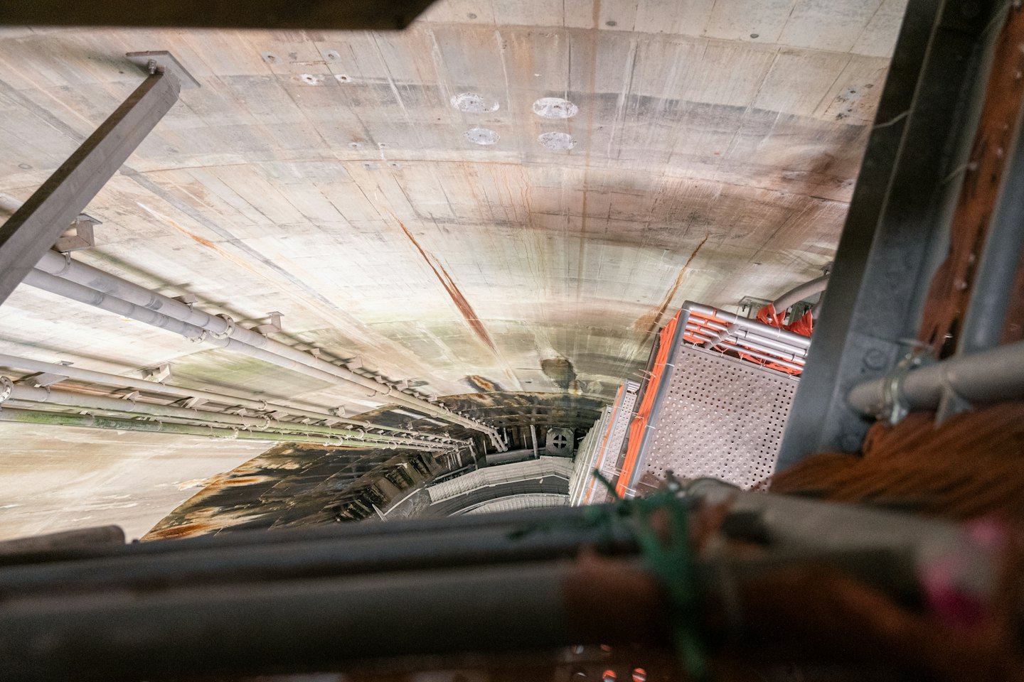 Tunnel industriale in cemento con tubi e ponteggi metallici lungo le pareti.